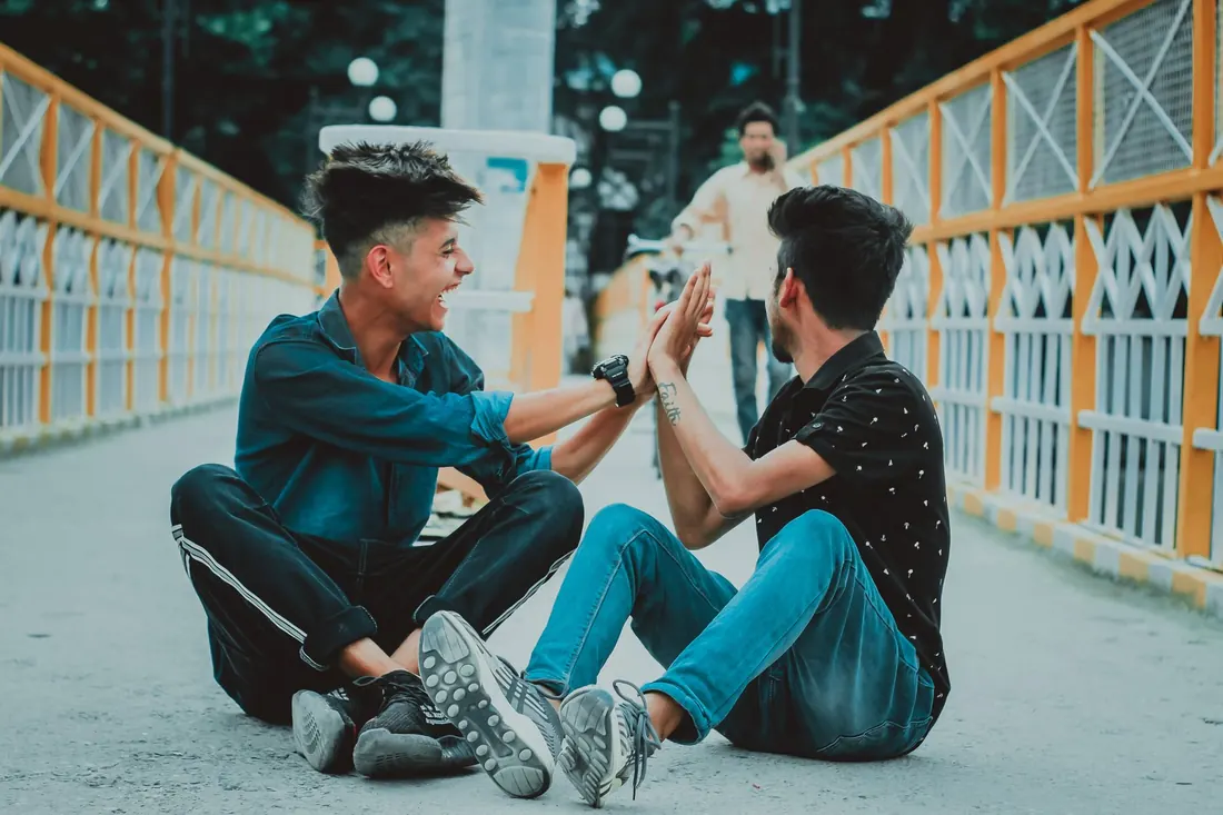 Two friends sitting on a bridge, laughing and high-fiving