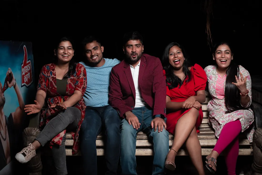 Five friends laughing together on a bench at night