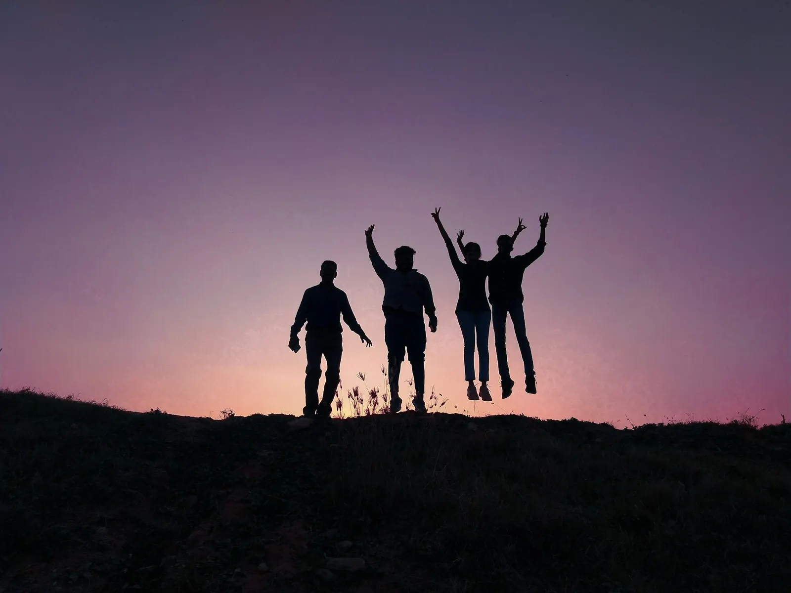 Four friends jumping on a hilltop at sunset, seen as silhouettes