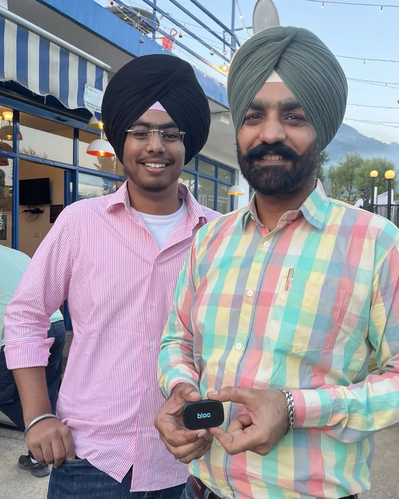 Two smiling members at a hillside cafe at dusk, the older one holding his bloc toward the camera