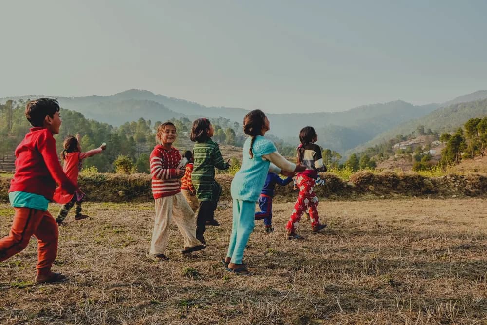 पहाड़ों के सामने खेत में दौड़ते और खेलते बच्चे