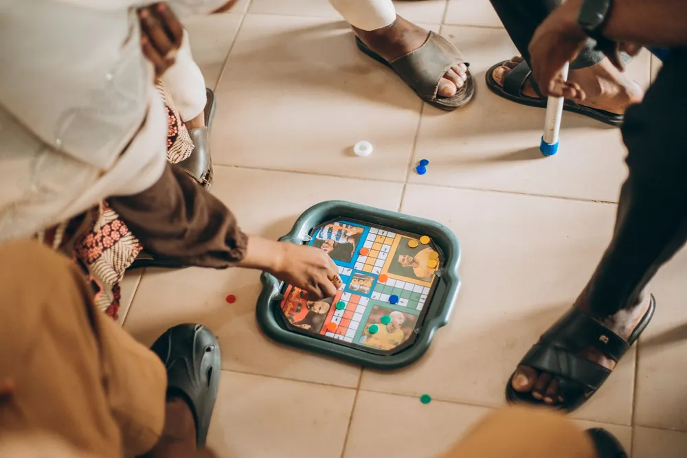 ज़मीन पर बैठकर साथ में ludo खेलता परिवार