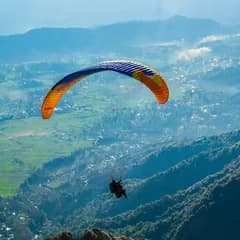 A paraglider over green valleys in Himachal