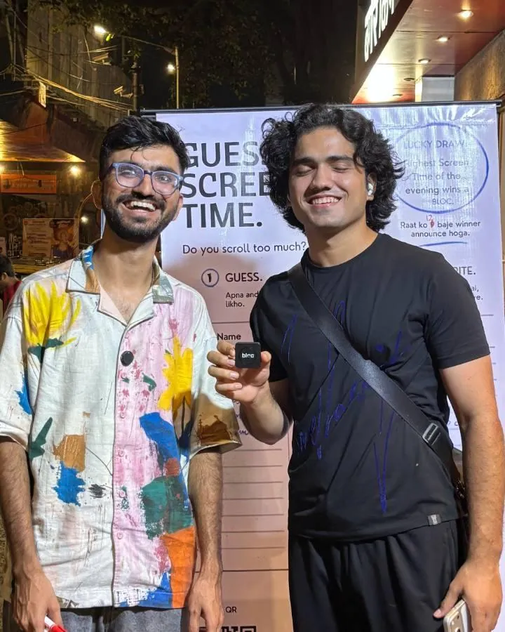 Two young men smiling at the board in Lower Parel at night, one holding a bloc