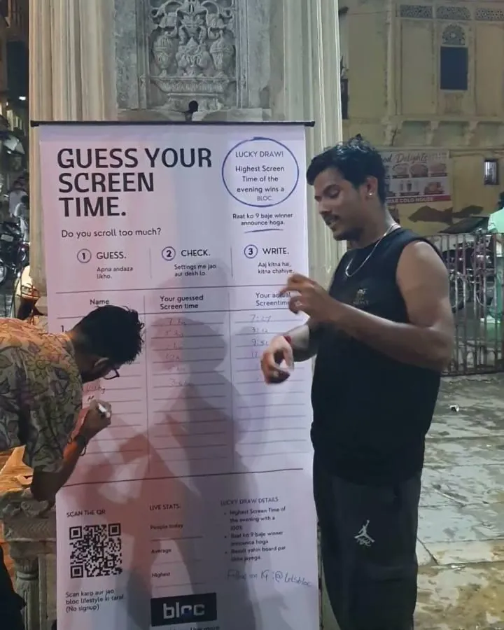 A man in a black vest at the board at Gangaur Ghat while a number is written down